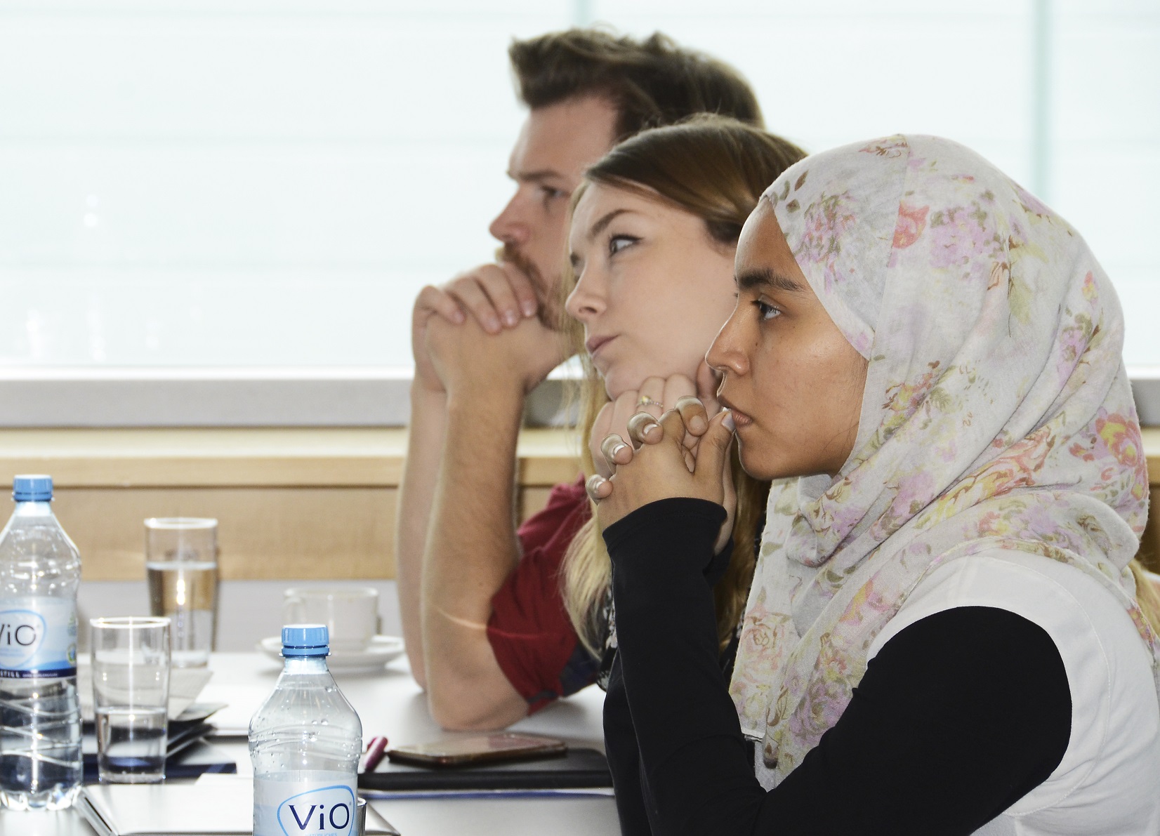 Three people sitting on a table in a row and listening to something